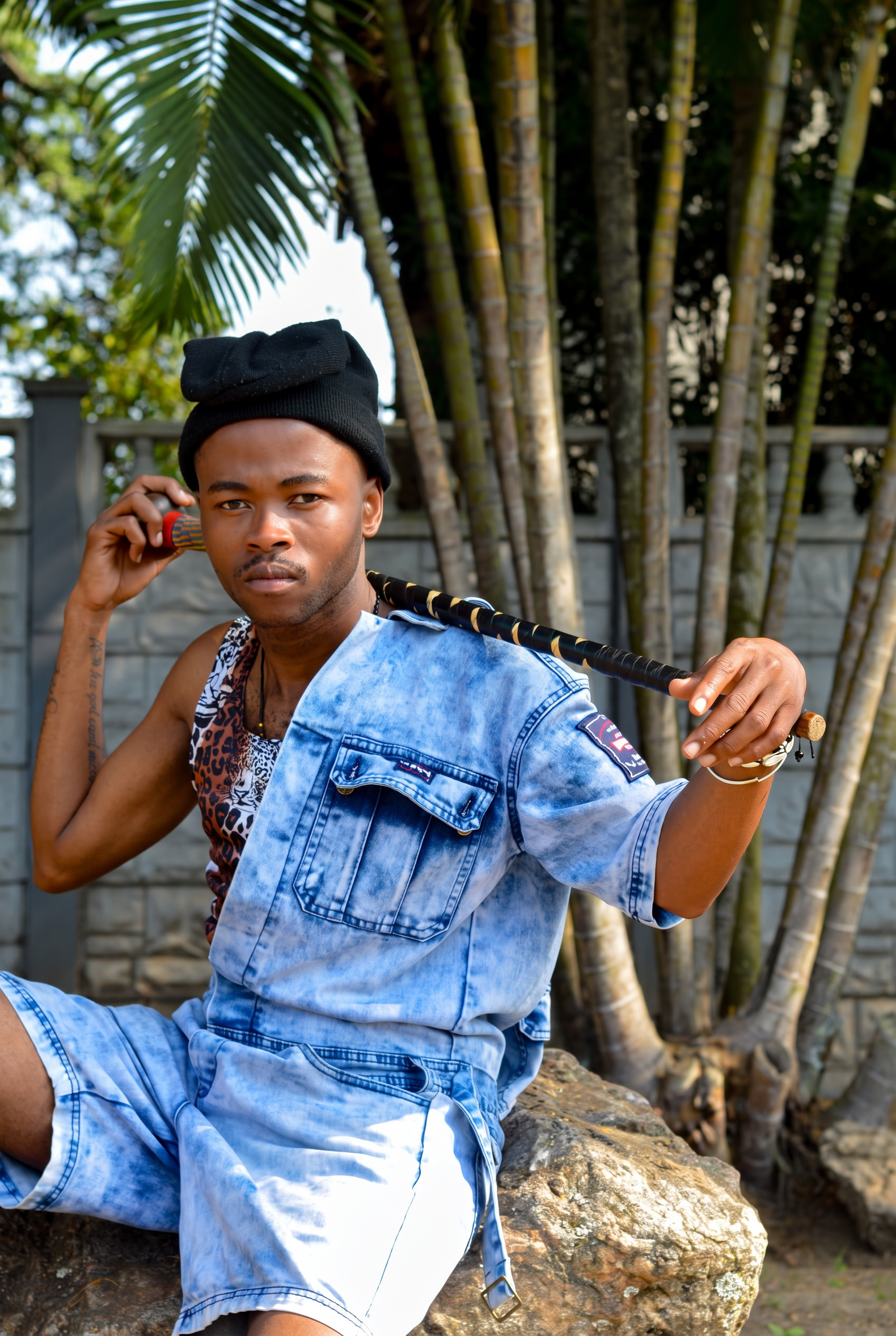 LatshuZAR in denim, seated with a traditional stick